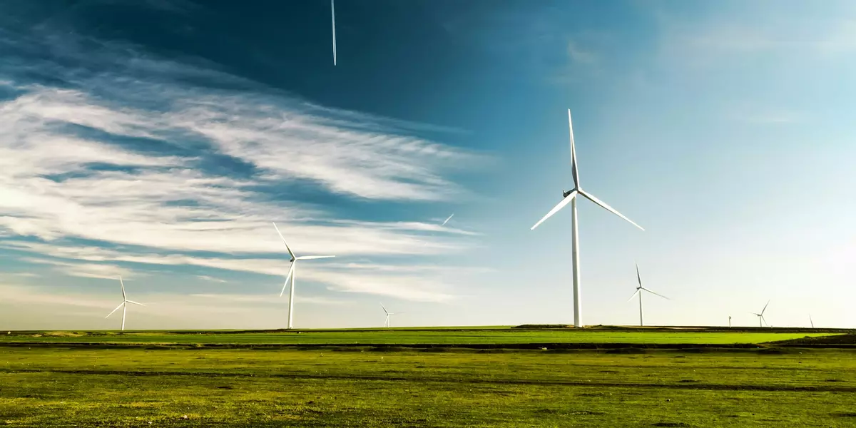 mehrere Windkraftanlagen auf einem grünen Feld vor blauem Himmel.