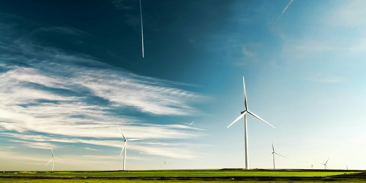 mehrere Windkraftanlagen auf einem grünen Feld vor blauem Himmel.