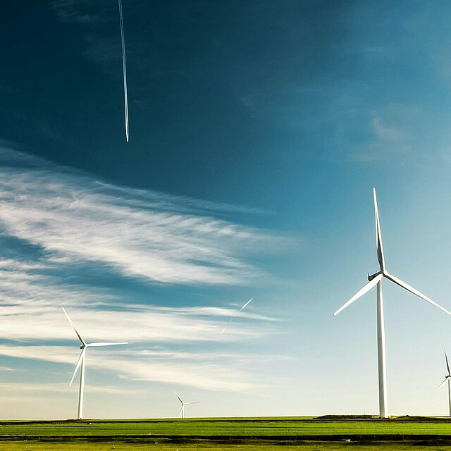 mehrere Windkraftanlagen auf einem grünen Feld vor blauem Himmel.