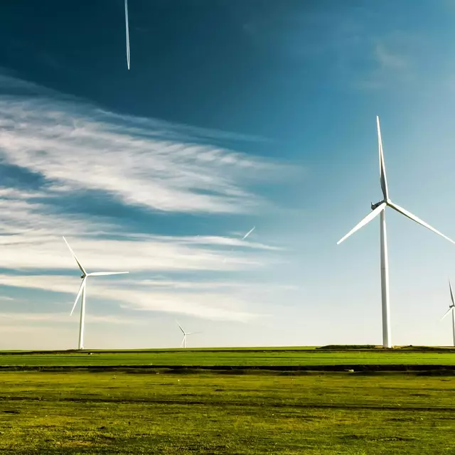 mehrere Windkraftanlagen auf einem grünen Feld vor blauem Himmel.