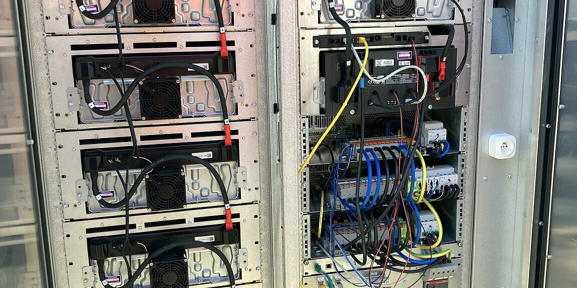 Geöffneter Batteriespeicher-Schrank mit neun Batteriemodulen (linke Schaltschrankseite + rechte obere Hälfte), dem Batteriemanagementsystem, drei Wechselrichtereinheiten und dem Steuerschrankmodul.